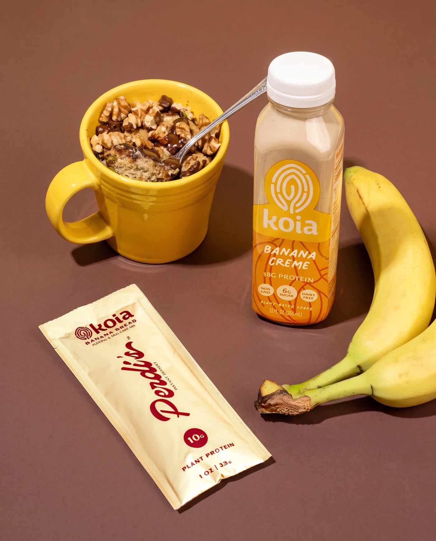 Perdi's Banana Bread packet beside a banana bread mug cake, a bottle of Koia Banana Creme, and bananas